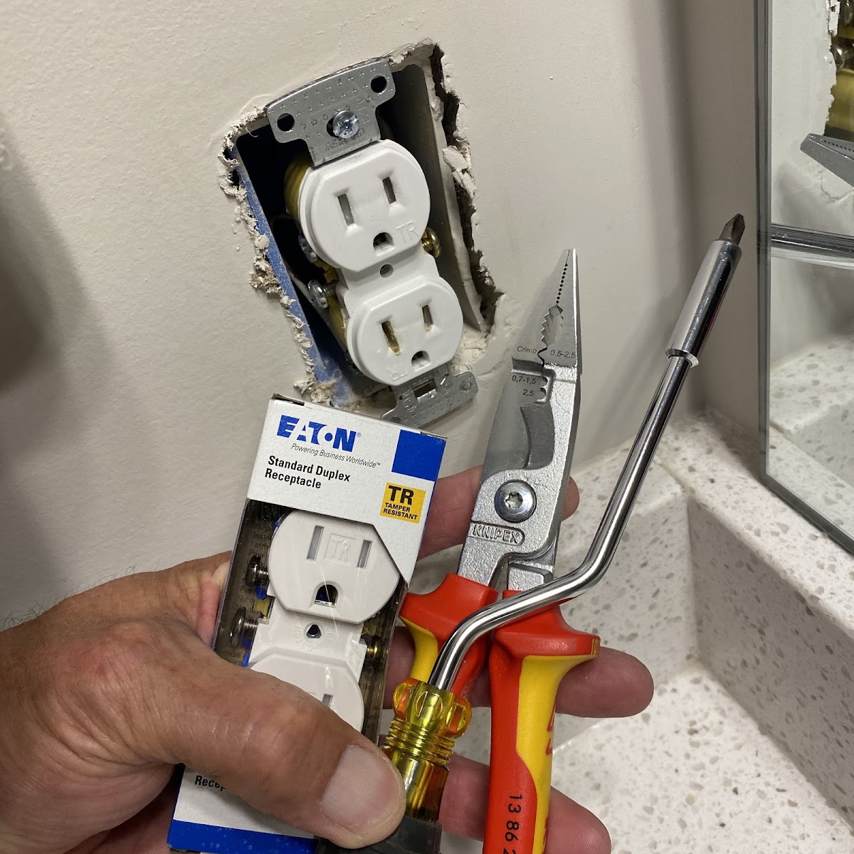 Hand holding a new electrical outlet and pliers